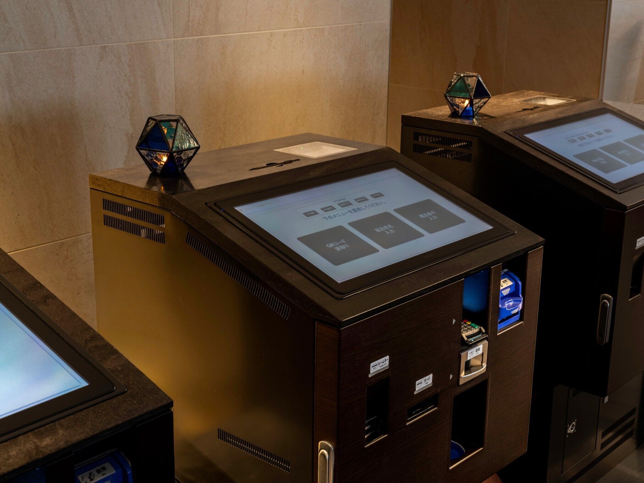 A row of self-service kiosks with a digital display, card reader, and a small decorative item on top.