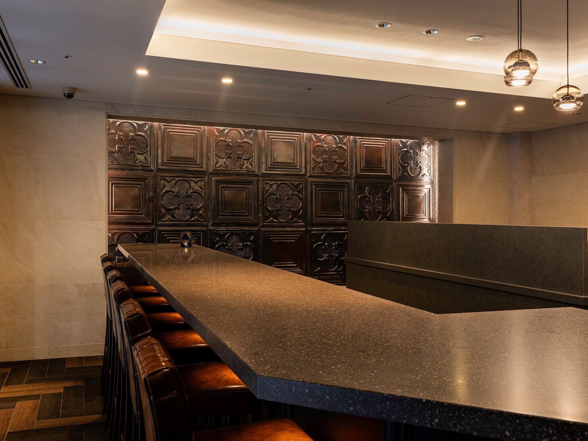 Uma área de bar com um balcão comprido, banquetas e painéis decorativos na parede.