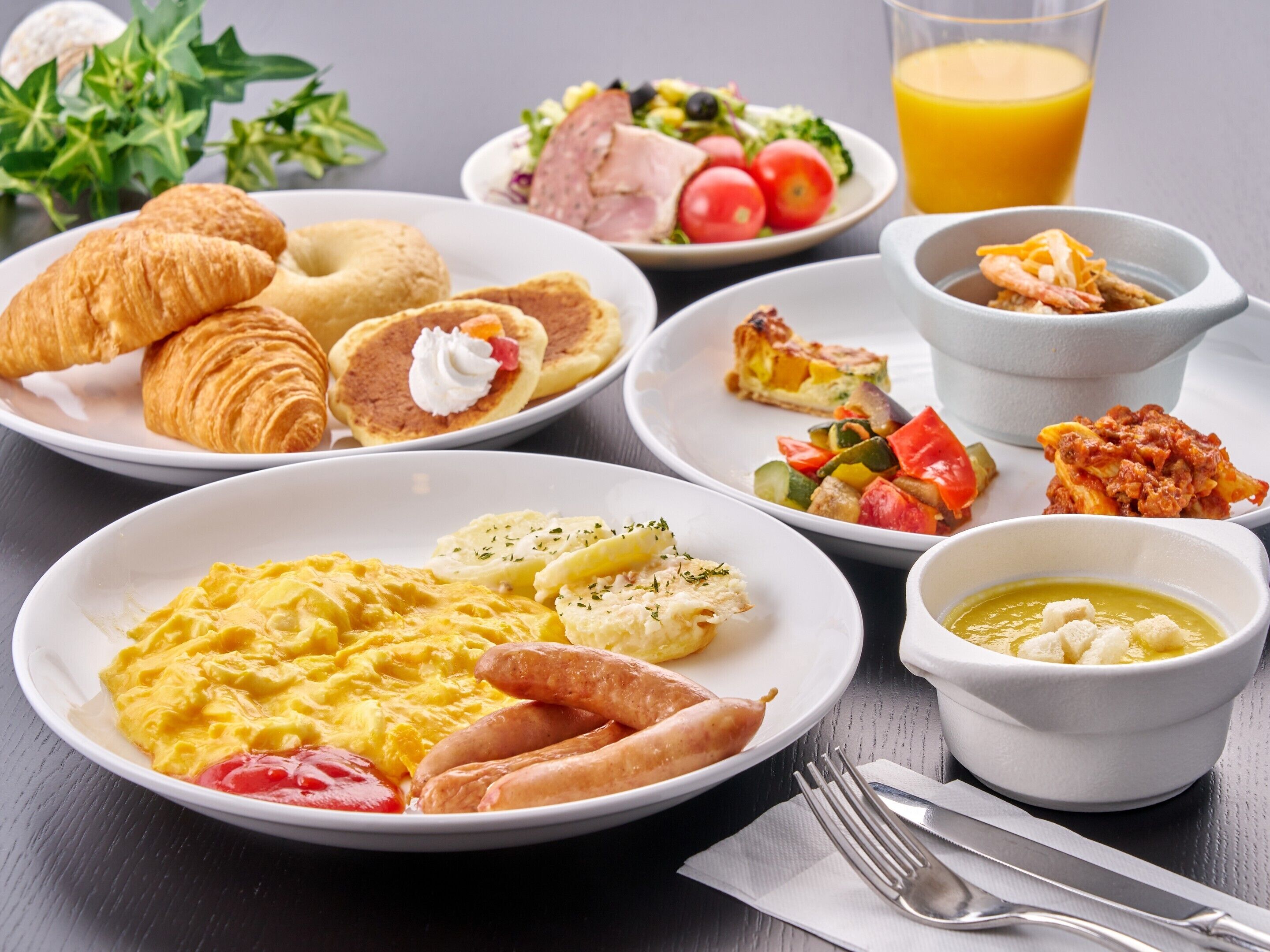 A breakfast spread with croissants, eggs, sausages, and various dishes.