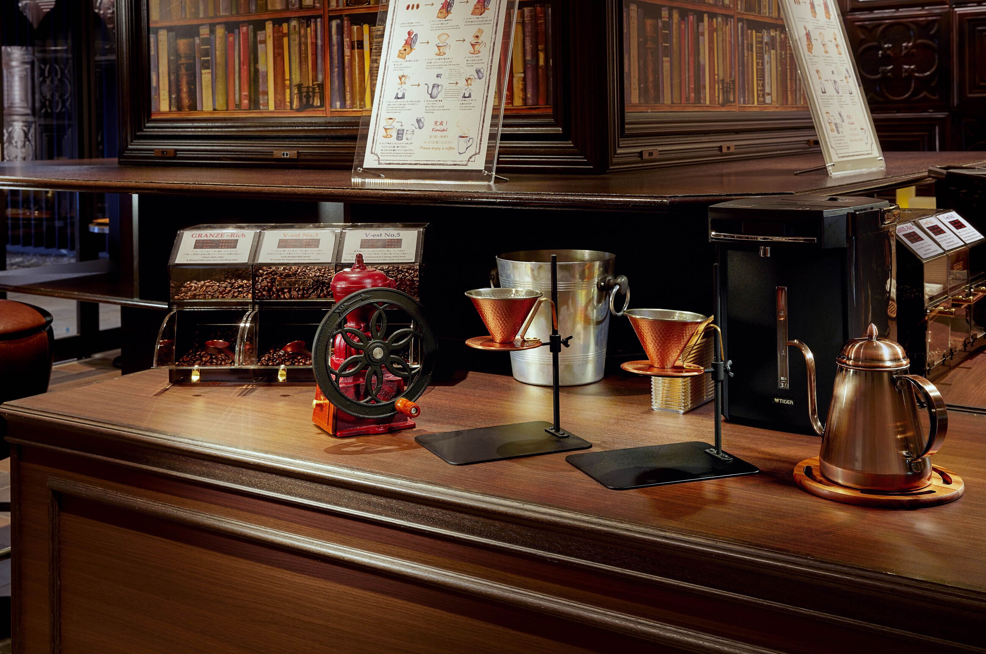 A coffee shop counter with brewing equipment, a menu stand, and a bookshelf in the background.