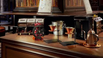 A coffee shop counter with brewing equipment, a menu stand, and a bookshelf in the background.