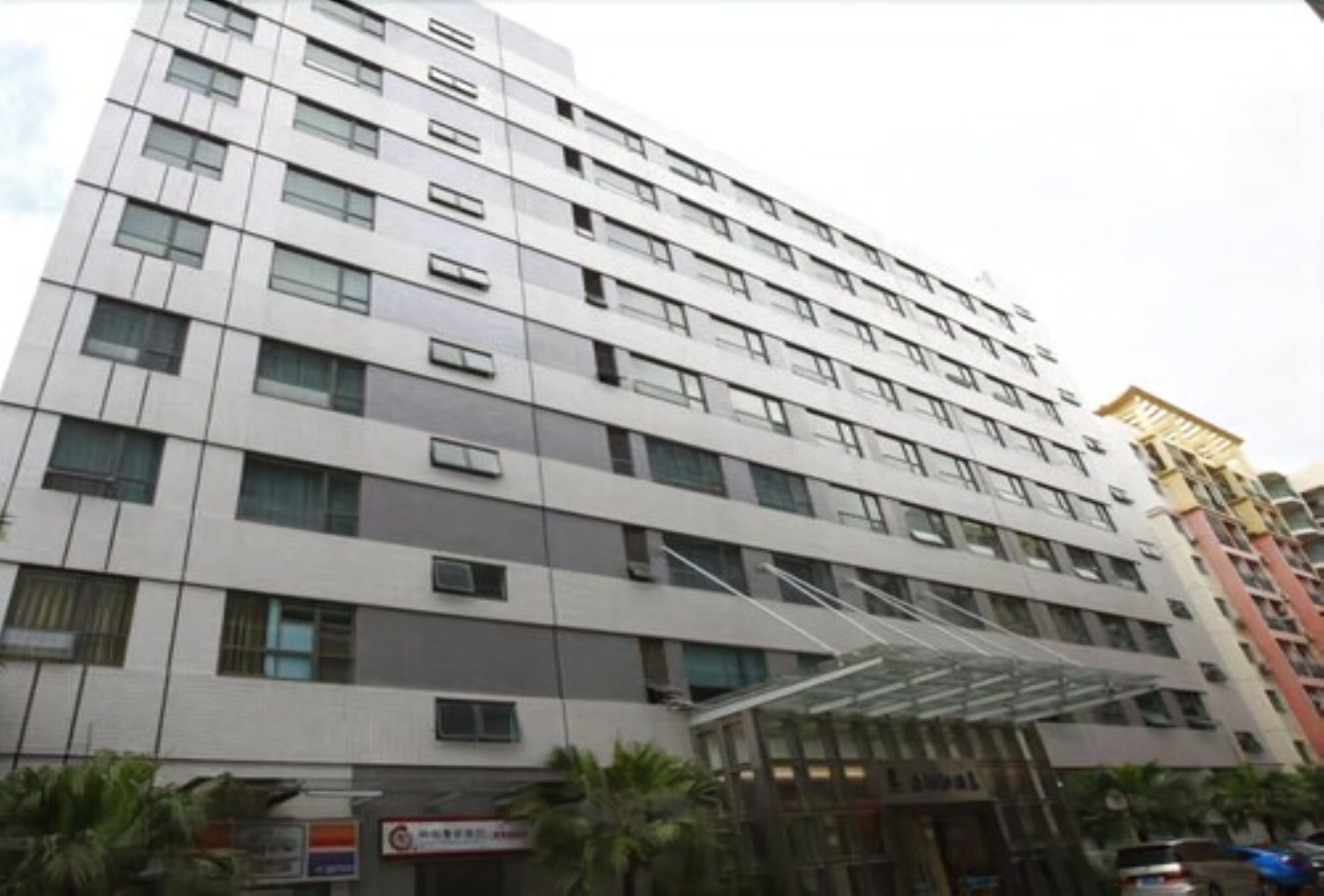 Un hotel de varios pisos con un diseño moderno, que cuenta con una entrada de vidrio y múltiples balcones.