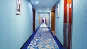 Un couloir d’hôtel avec un tapis à motifs, des portes en bois et des tableaux encadrés accrochés aux murs.