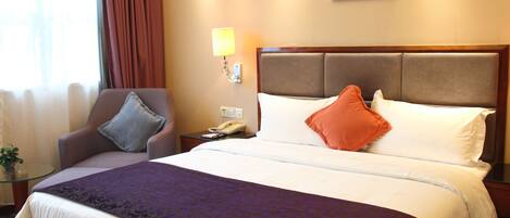 A hotel room with a large bed, a chair, a bedside table with a lamp, and a painting on the wall.