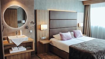 Una habitación de hotel moderna con una cama grande, un espejo redondo, una mesita de noche con una lámpara y un lavamanos integrado.