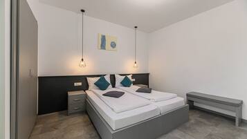 Une chambre moderne avec un grand lit, des tables de chevet, un banc et des lampes suspendues.