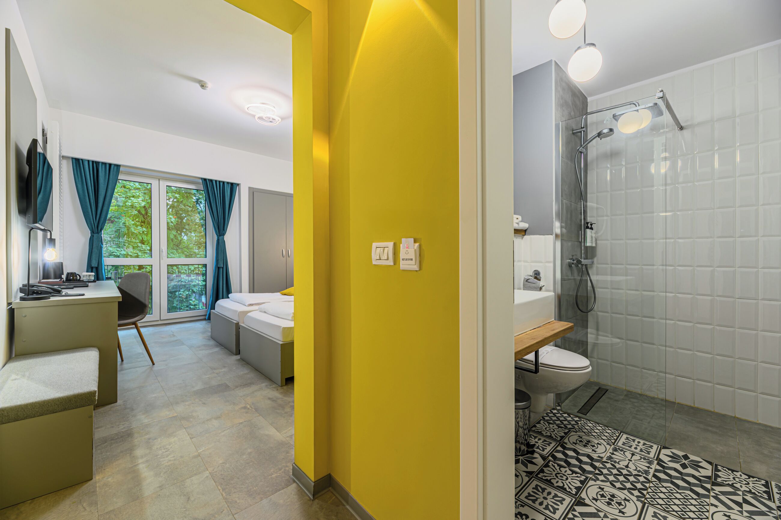 Quarto de hotel moderno com uma cama, uma escrivaninha e um banheiro com chuveiro.