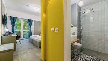 Quarto de hotel moderno com uma cama, uma escrivaninha e um banheiro com chuveiro.