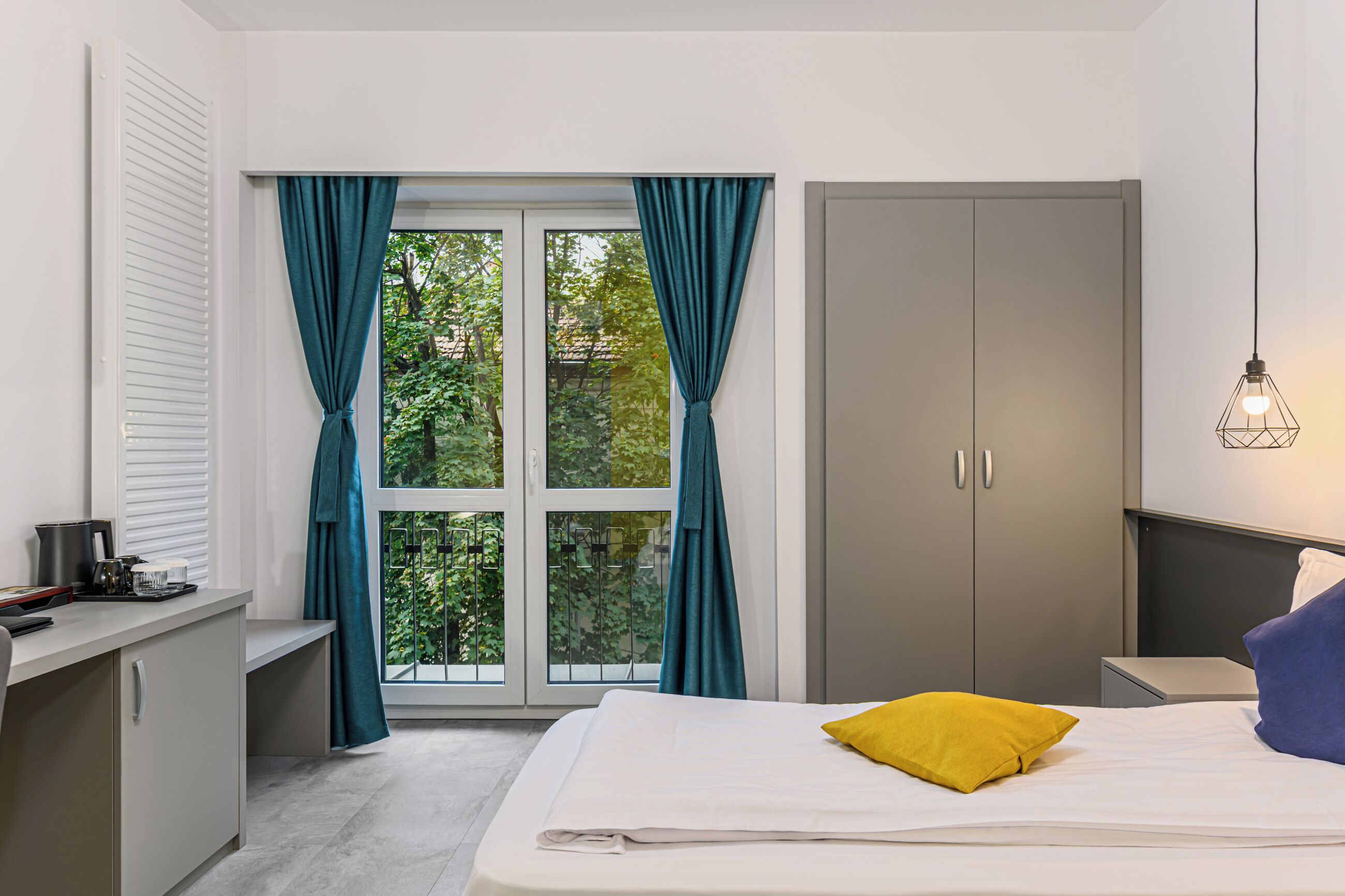 Un dormitorio con cama, escritorio, armario y ventana con cortinas.