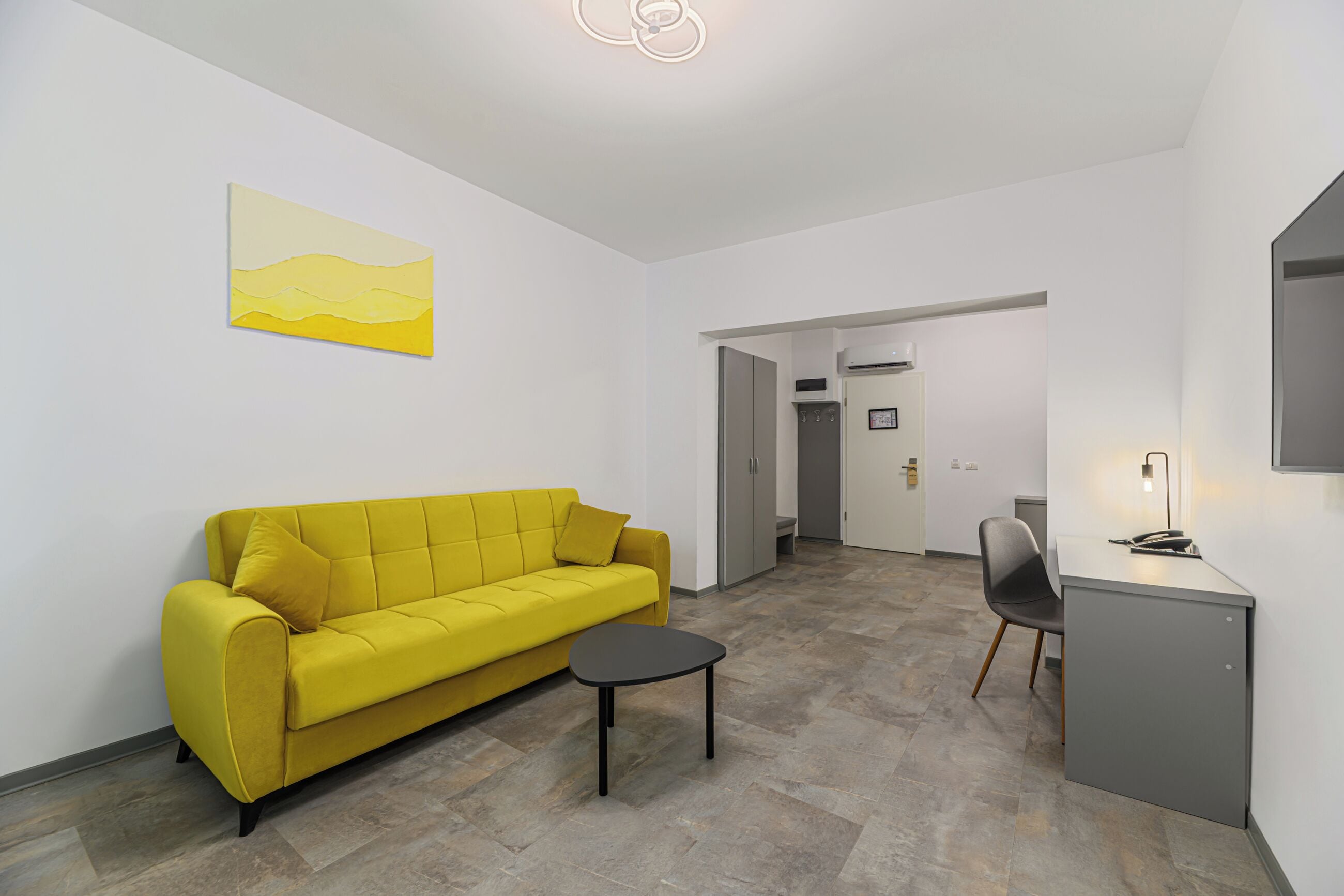 A modern living room with a yellow sofa, a small black table, and a grey cabinet.