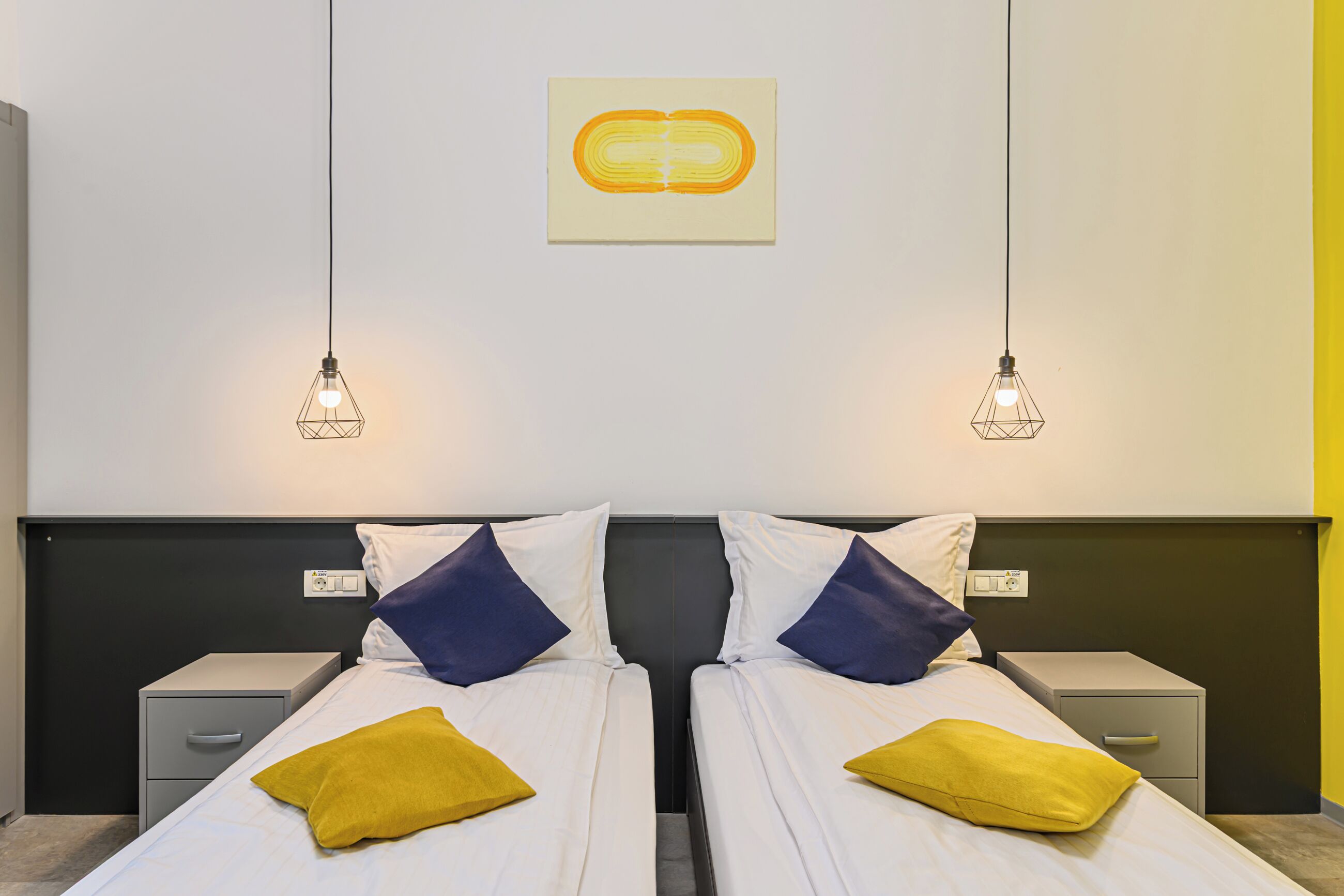 Een tweepersoonsbed met twee kussens, een nachtkastje en een wandlamp.