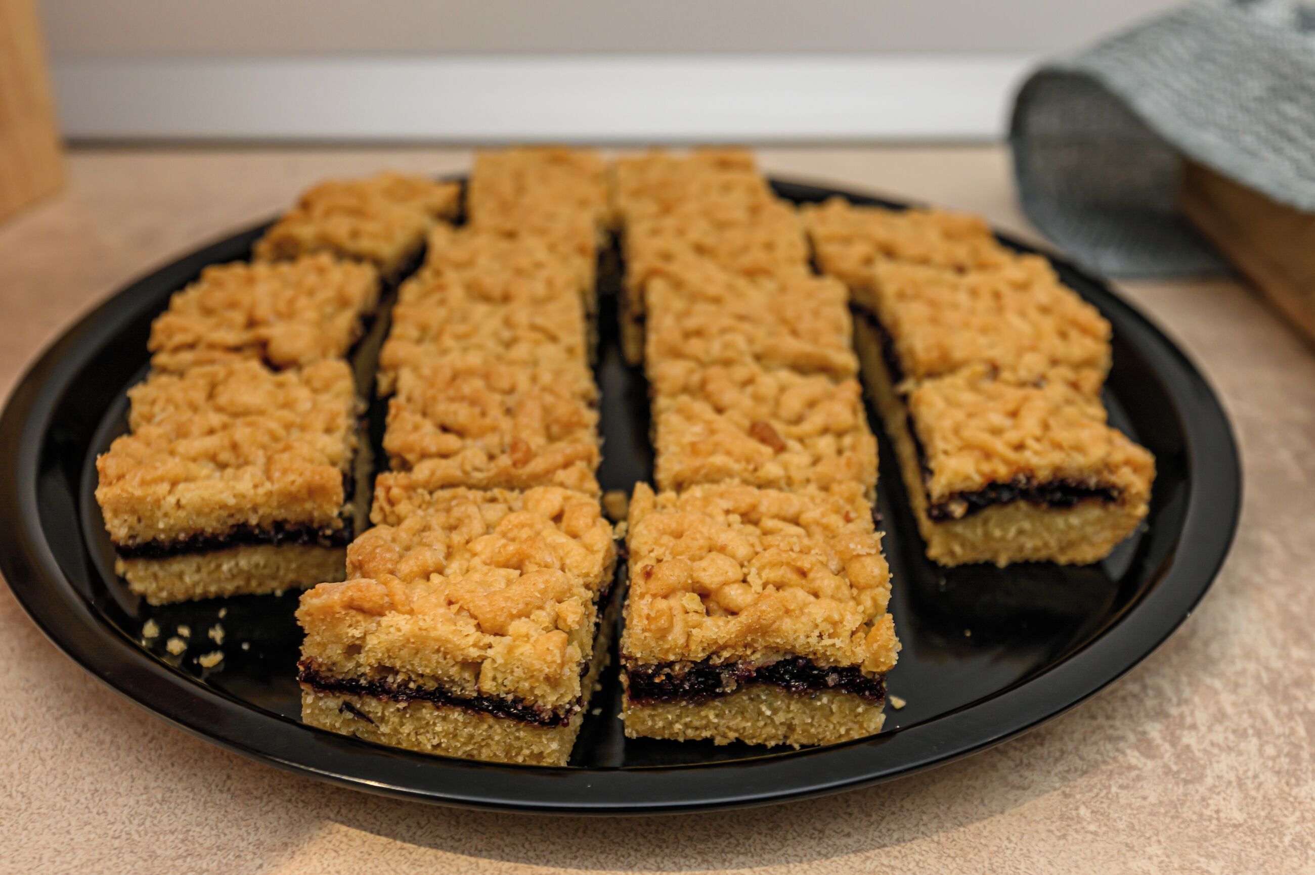 A plate of square-shaped dessert bars with a crumbly topping, arranged on a black plate.