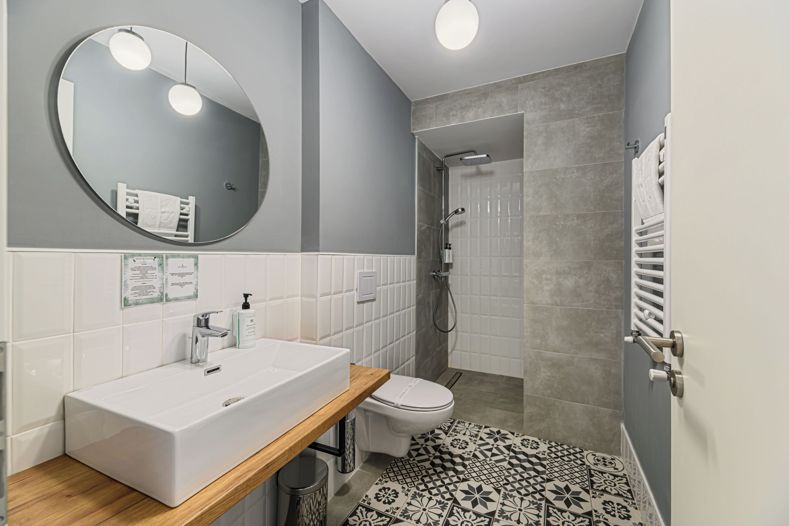 A modern bathroom with a large oval mirror, a rectangular sink, a toilet, and a shower area.