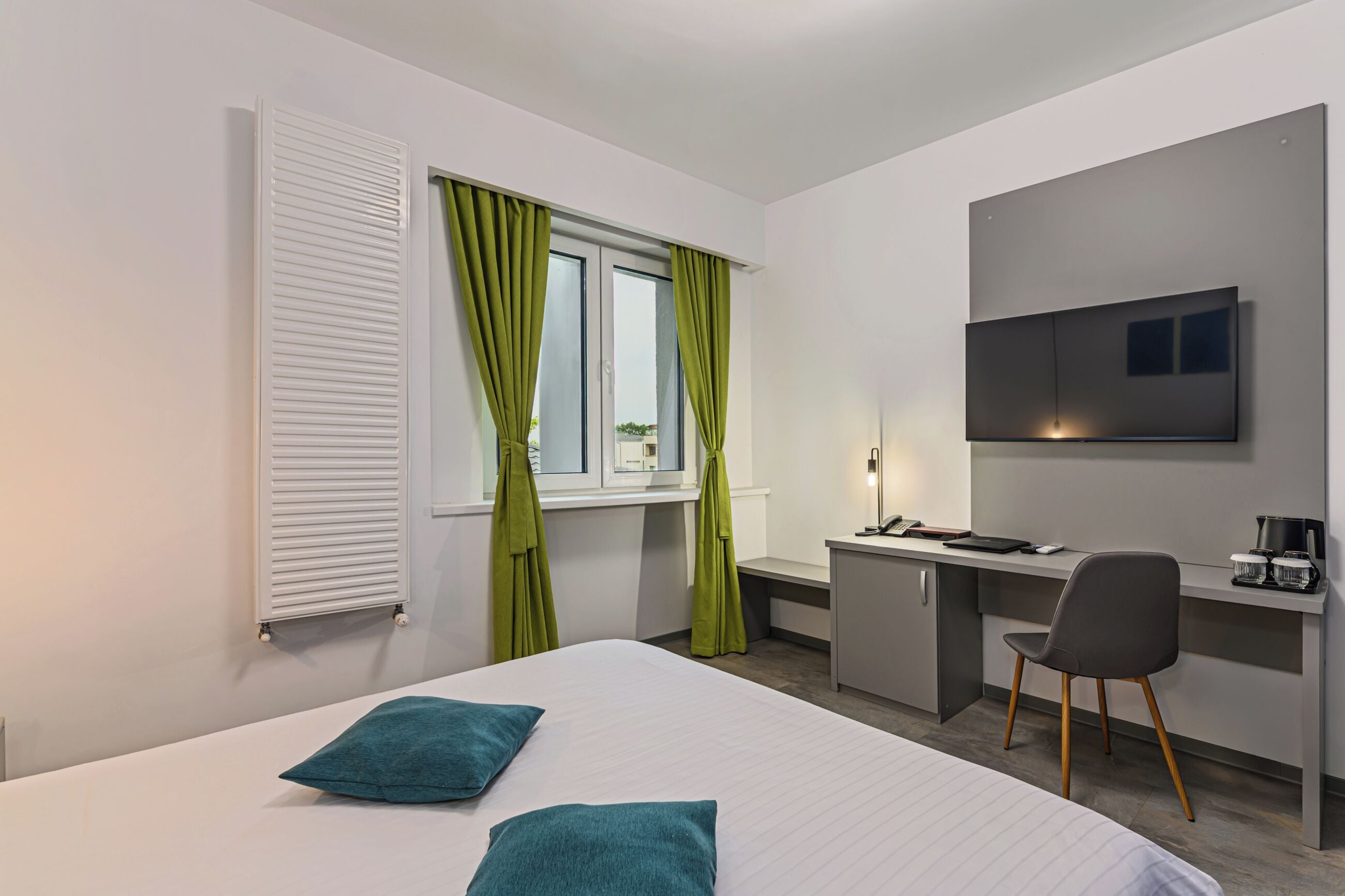 A modern hotel room with a bed, a desk, a chair, a television, and a window with curtains.