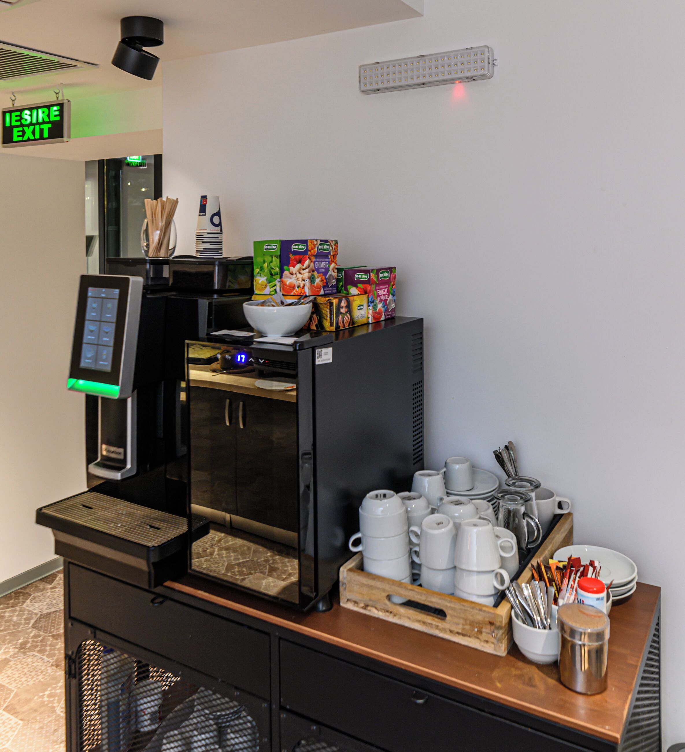A coffee station with a coffee machine, a bowl of utensils, and a tray of cups and mugs.