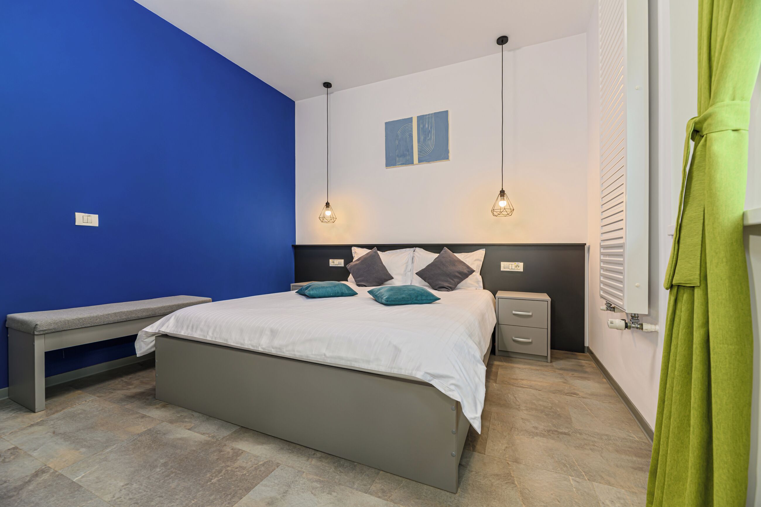 Un dormitorio con cama, banca, mesitas de noche y una cortina verde.