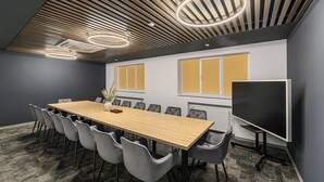 A conference room with a long table, grey chairs, a whiteboard, and a large screen. - Johann Strauss (Bucharest)