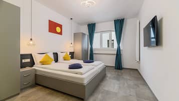 A modern bedroom with a bed, bedside tables, a wardrobe, a TV, and a window with curtains.