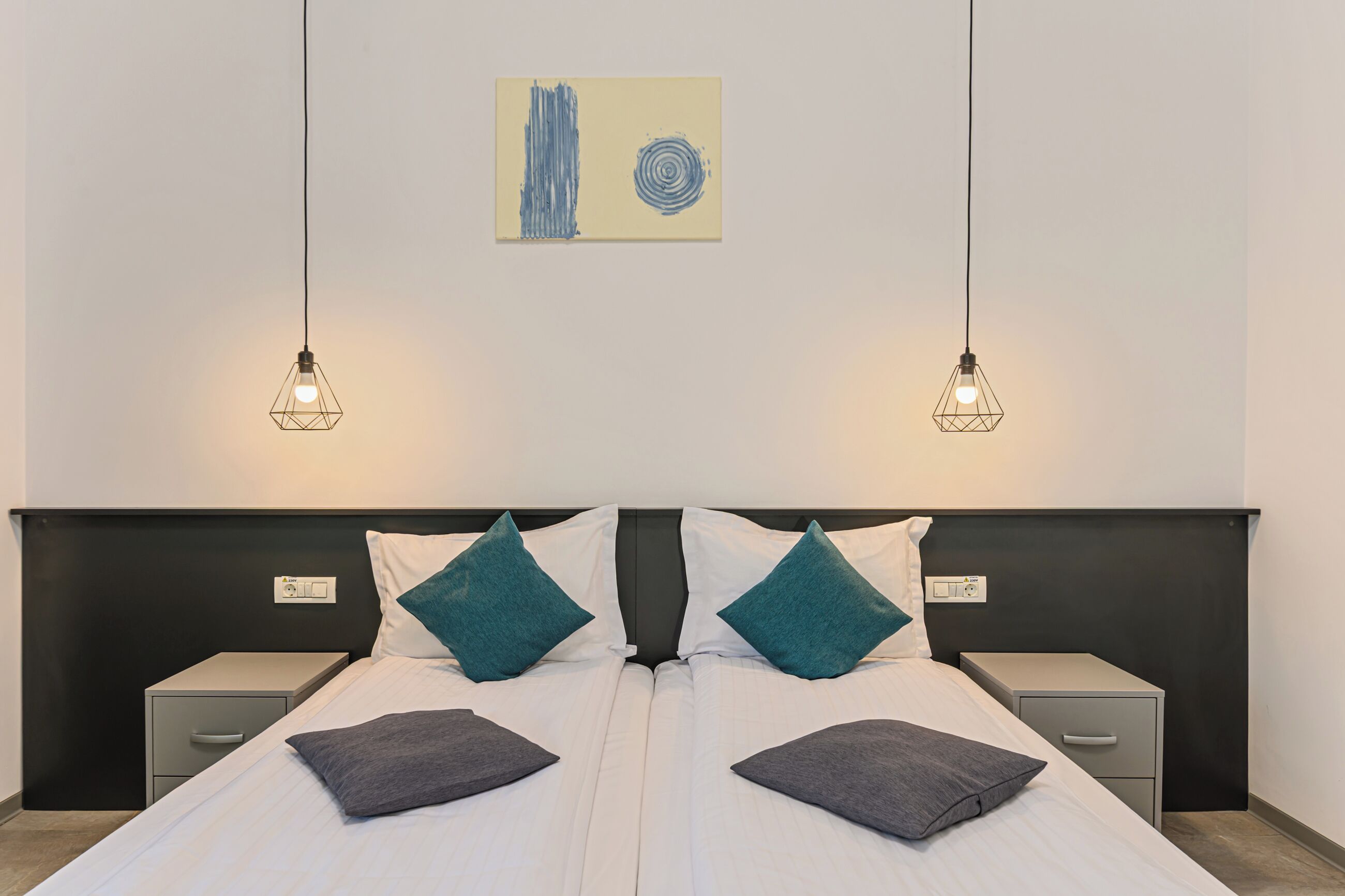 A double bed with two nightstands, each with a drawer, and a wall-mounted light fixture above.