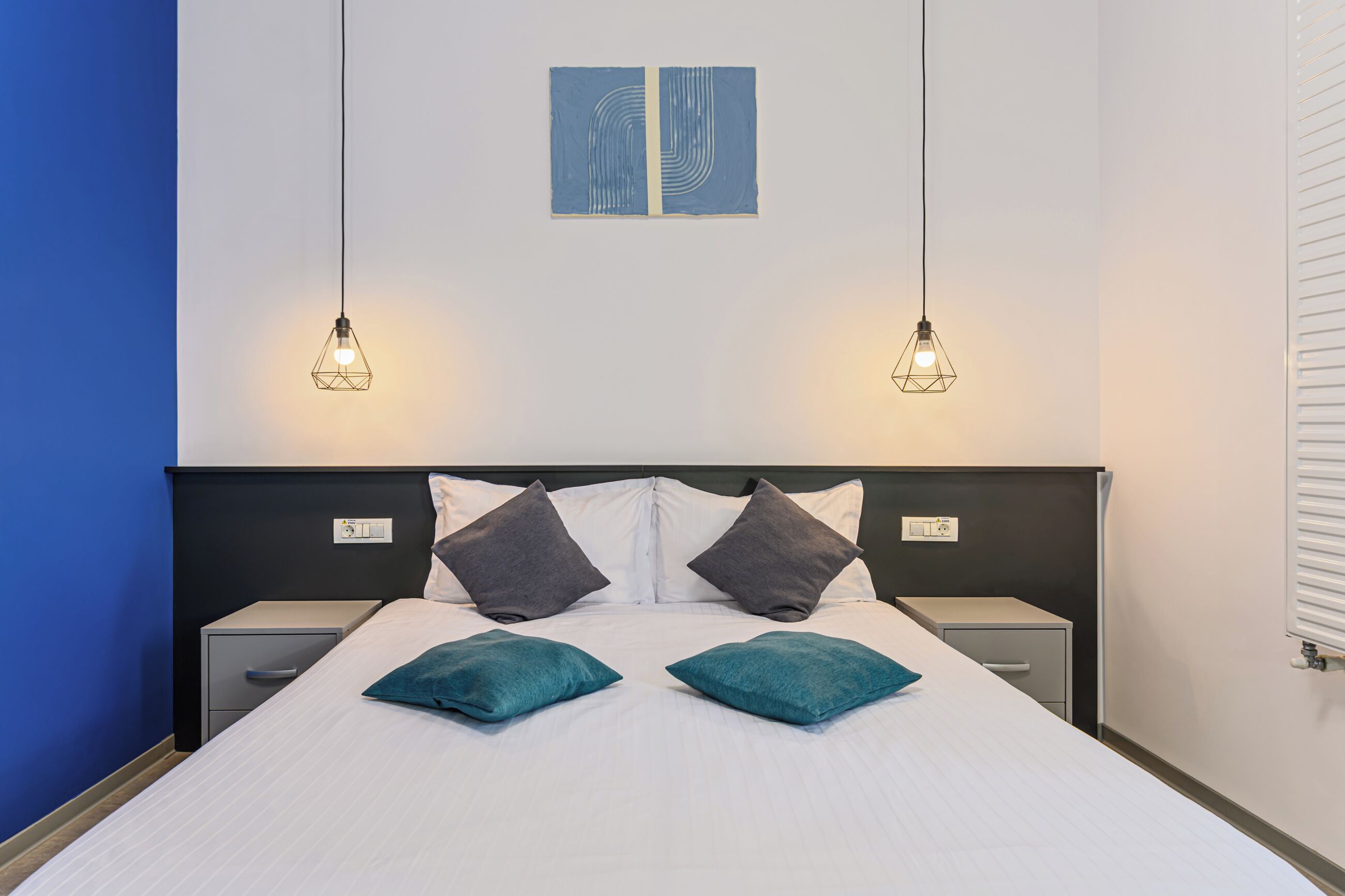 A neatly made bed with two pillows, a headboard, bedside tables, and wall art above.