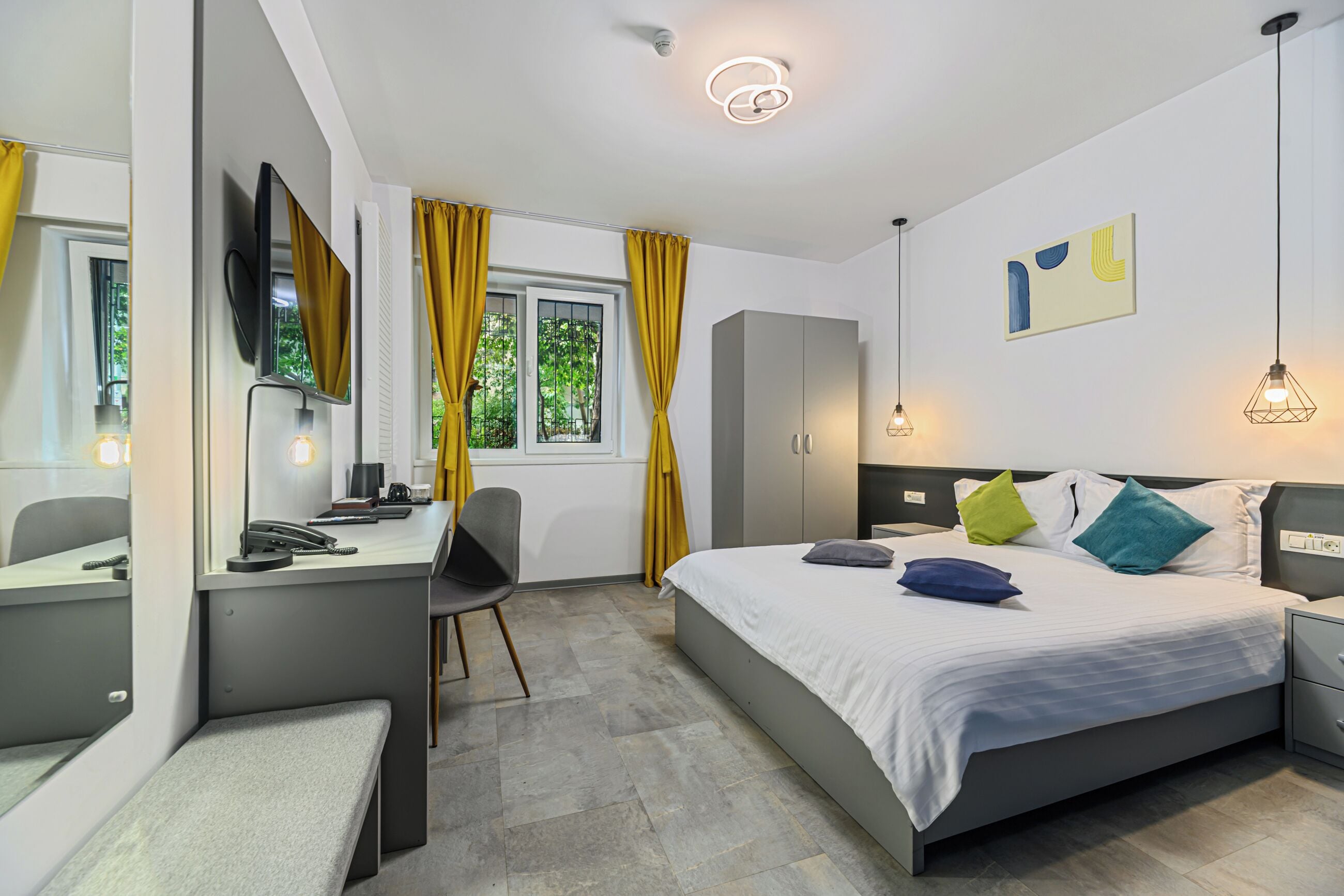 A modern hotel room with a bed, desk, chair, and wardrobe.