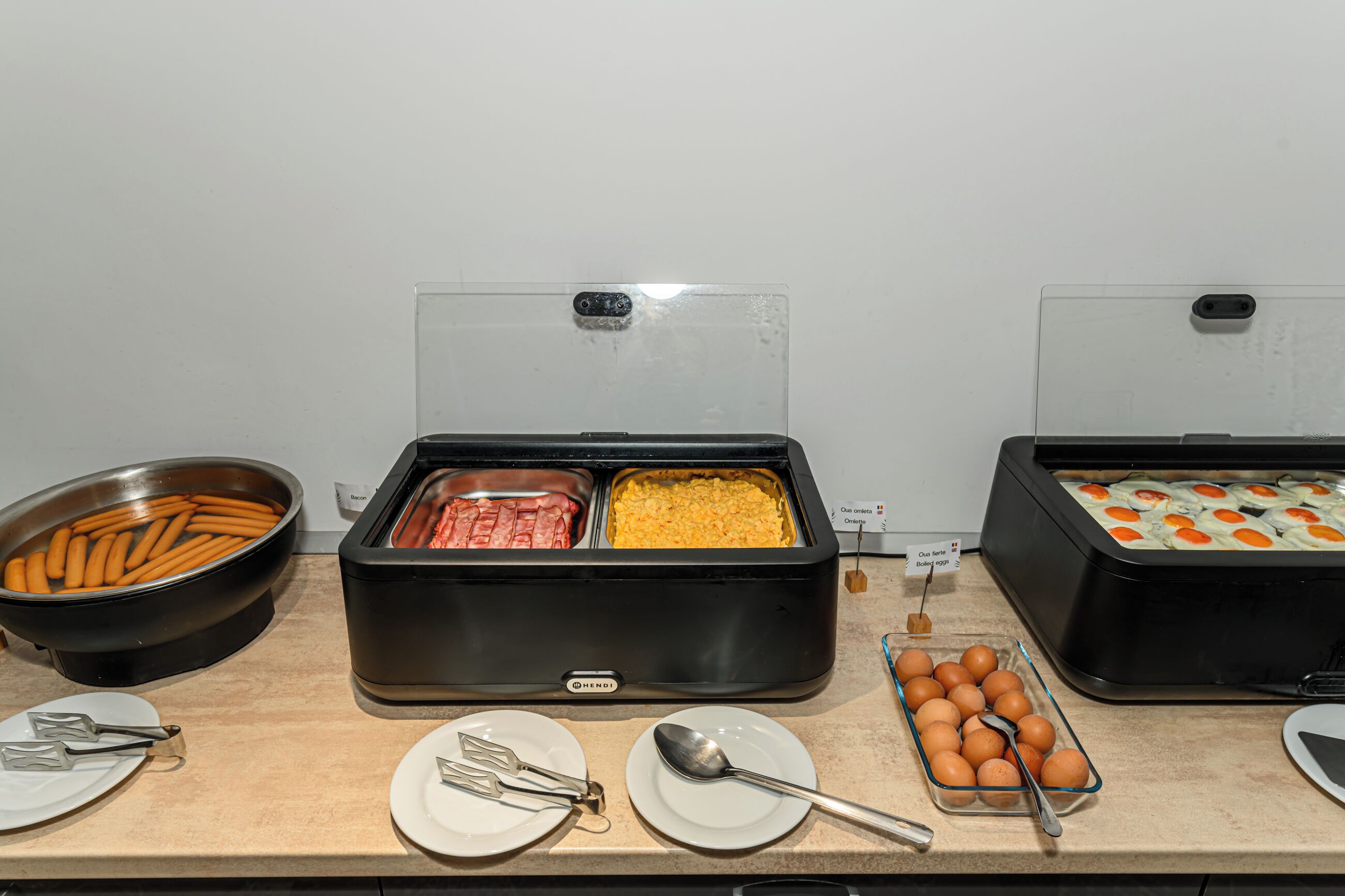 Montaje de buffet con diversos alimentos, como tocino, huevos revueltos y huevos cocidos.