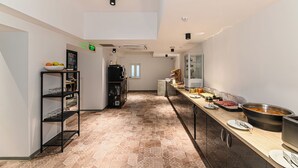 A modern kitchen with a long counter, a black shelving unit, and a variety of food items. - Johann Strauss (Bucharest)