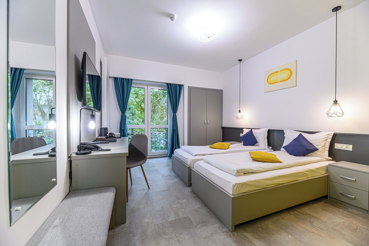 Una habitación de hotel moderna con escritorio, dos camas, una silla y un armario.
