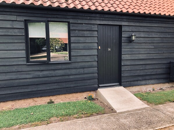 A black wooden building with a black door marked with the number 14, a window, and a small concrete step leading to the door.