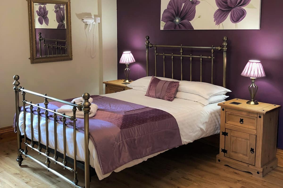 Een slaapkamer met een bed, nachtkastje, kaptafel, een kroonluchter, een spiegel en een bloemstillevordering aan de muur.