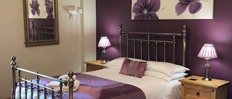 A bedroom with a bed, a nightstand, a dresser, a chandelier, a mirror, and a floral painting on the wall.
