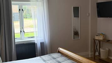 A bedroom with a bed, a window with curtains, a radiator, a television, and a chandelier.