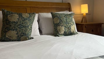 Una cama bien hecha con almohadones estampados de flores, un cabecero de madera y una mesita de noche con una lámpara.