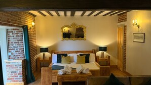 A cozy room with a wooden bed, two bedside tables, a mirror, and a brick wall. - The Farmhouse at Fincham (King's Lynn)