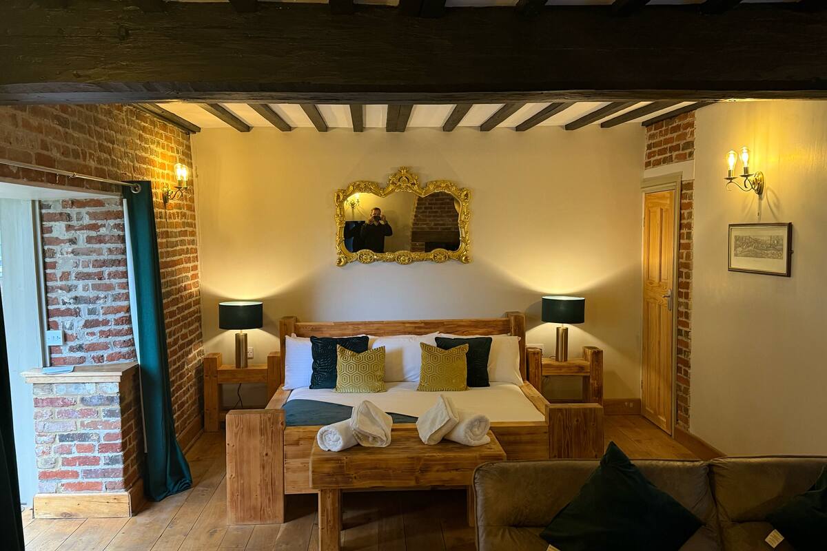 Een gezellige kamer met een houten bed, twee nachtkastjes, een spiegel en een bakstenen muur.