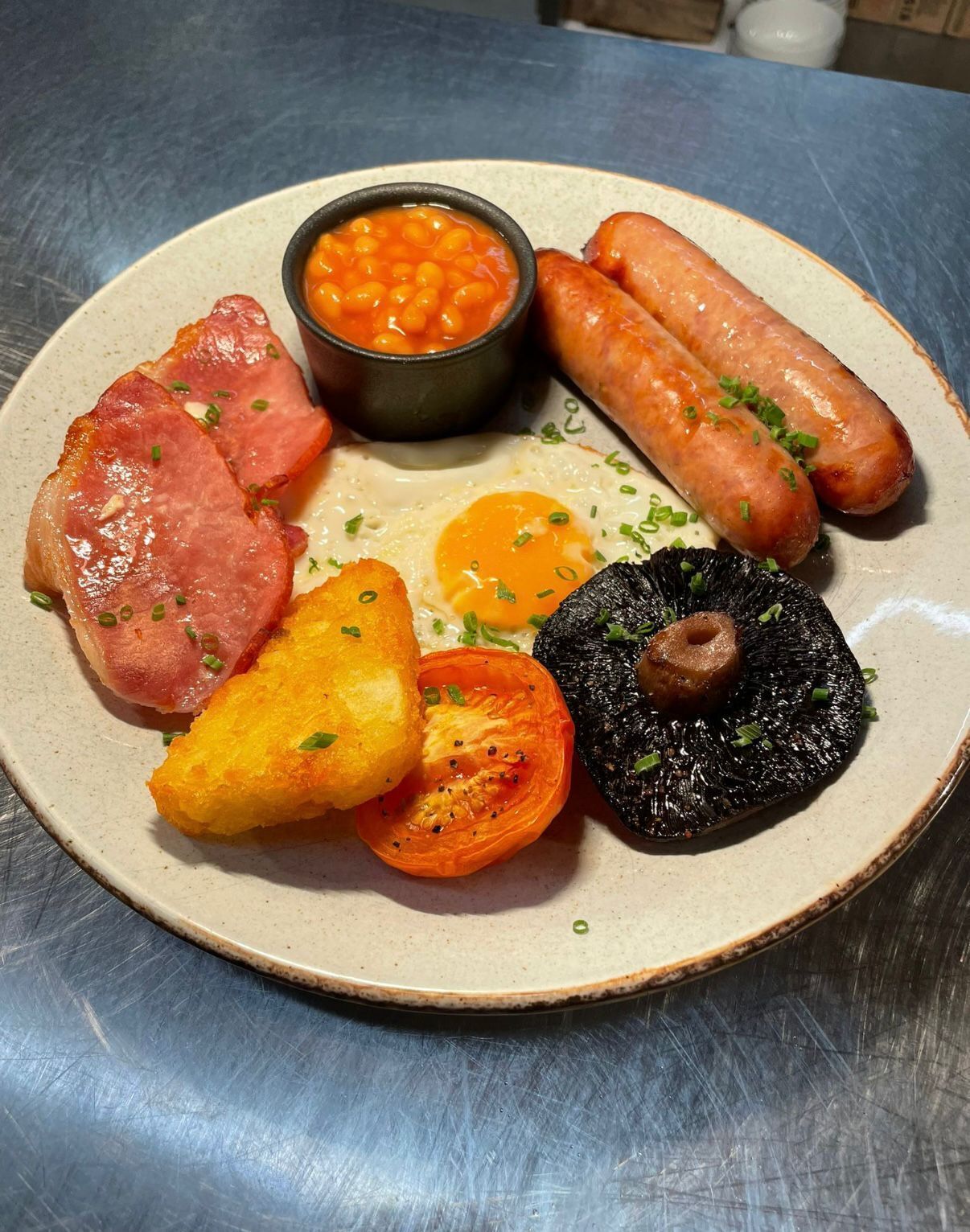 A plate with various breakfast items including sausages, eggs, bacon, baked beans, and a grilled tomato.