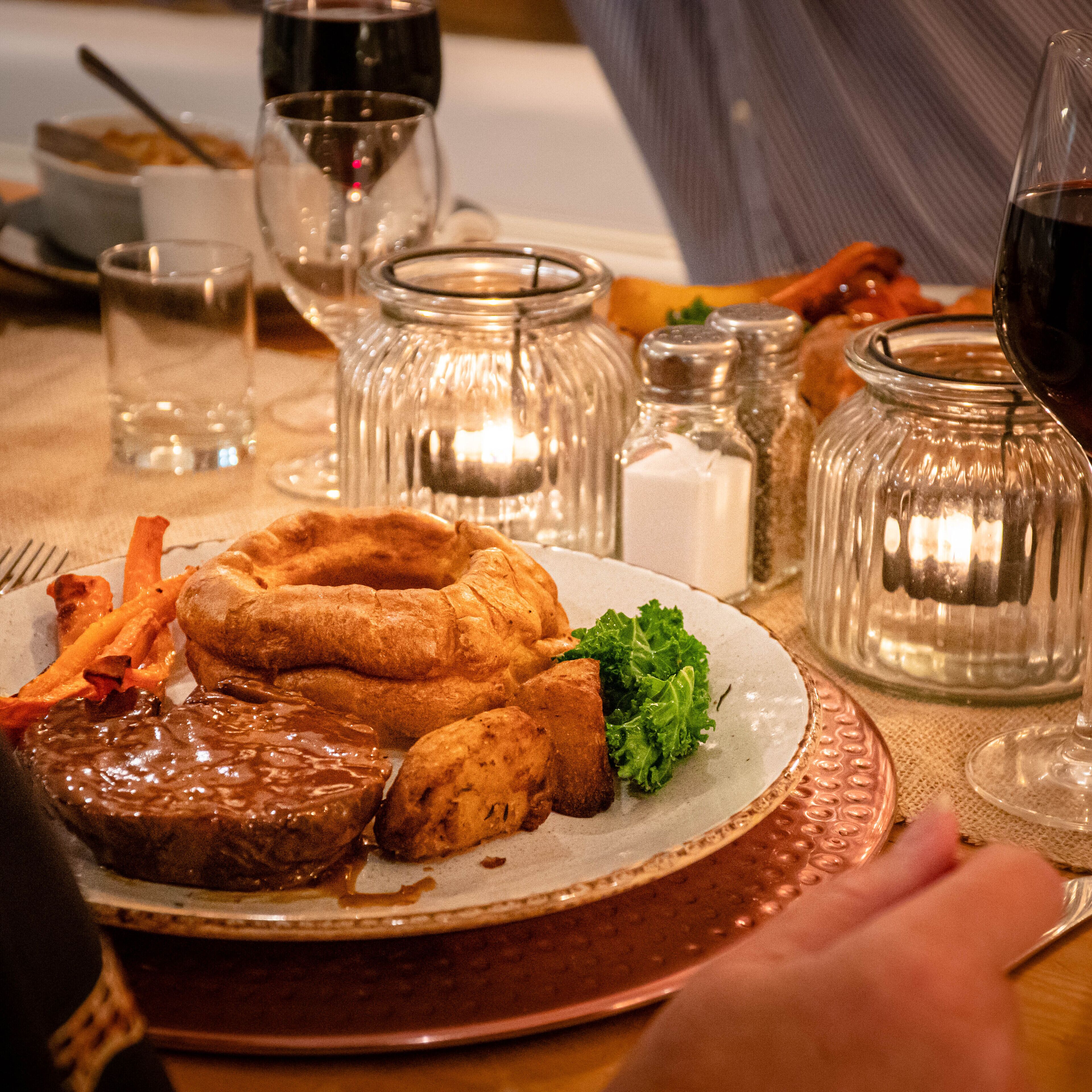 A dining table with a plate of food, glasses, and salt and pepper shakers.