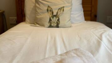 Una cama con ropa blanca y una almohada con estampado de conejo.
