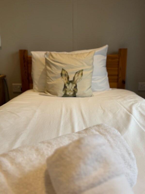 Una cama con ropa blanca y una almohada con estampado de conejo.
