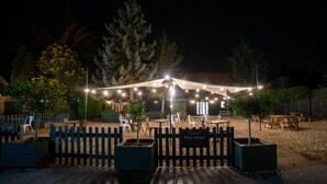 An outdoor seating area with tables and chairs under a canopy, surrounded by a wooden fence and trees. - The Farmhouse at Fincham (King's Lynn)