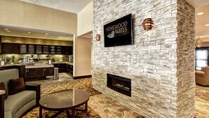 Uma sala de estar moderna com lareira de pedra, televisão na parede e cozinha ao fundo.