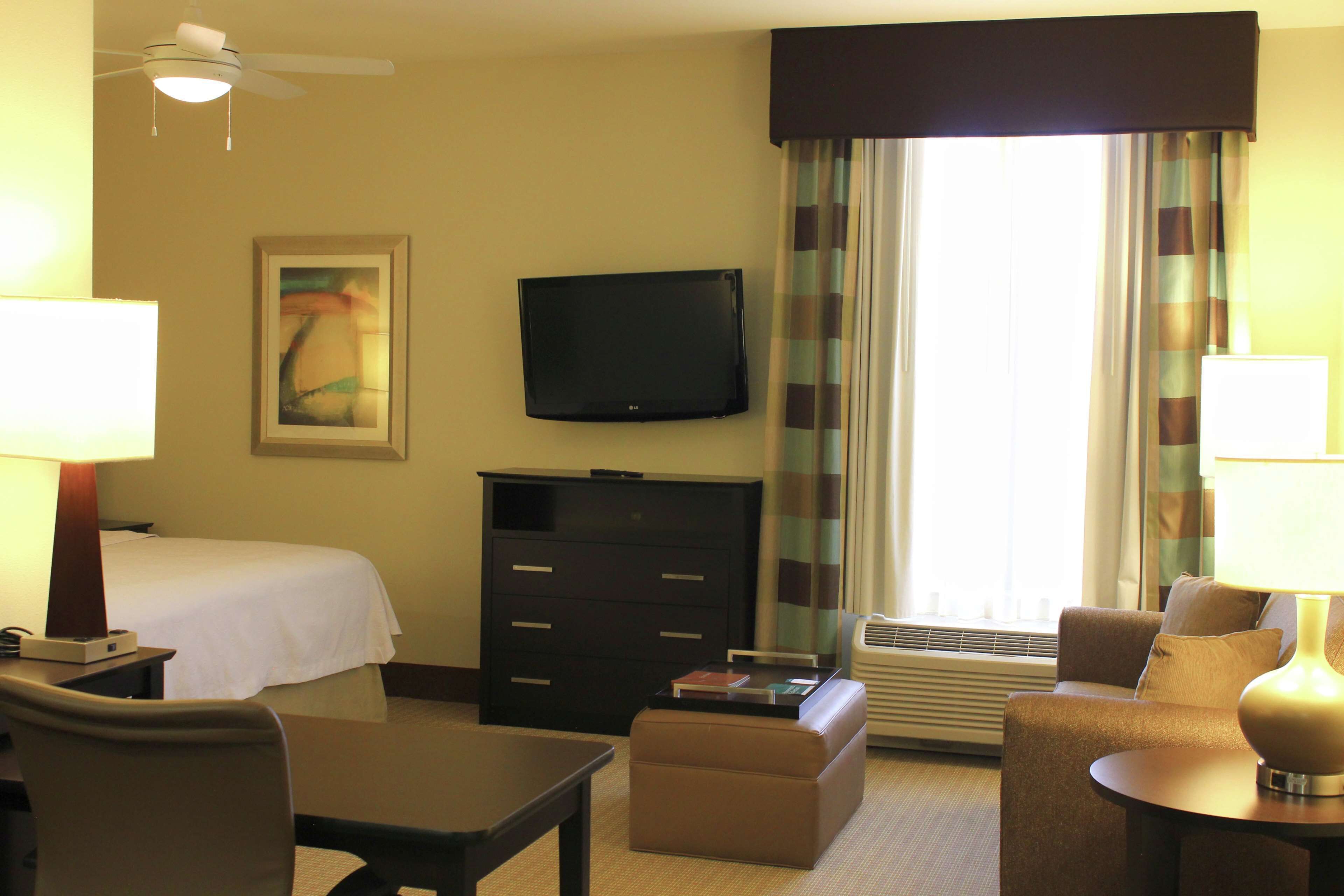 A hotel room with a bed, a desk, a chair, a television, a dresser, and a window with curtains.