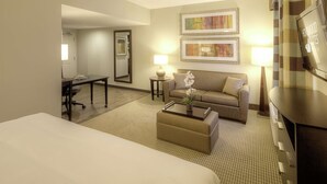 Quarto de hotel com cama, sofá, mesa de centro, escrivaninha e televisão.