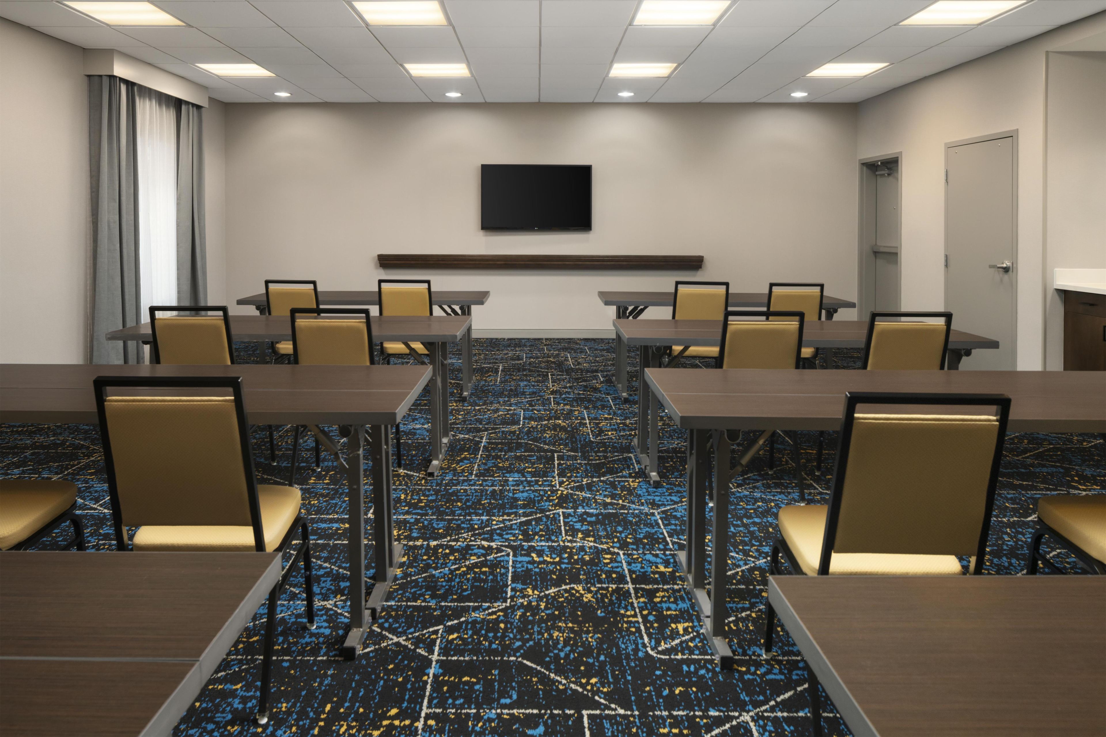 A conference room with a long table, chairs, a flat-screen TV, and a patterned carpet.