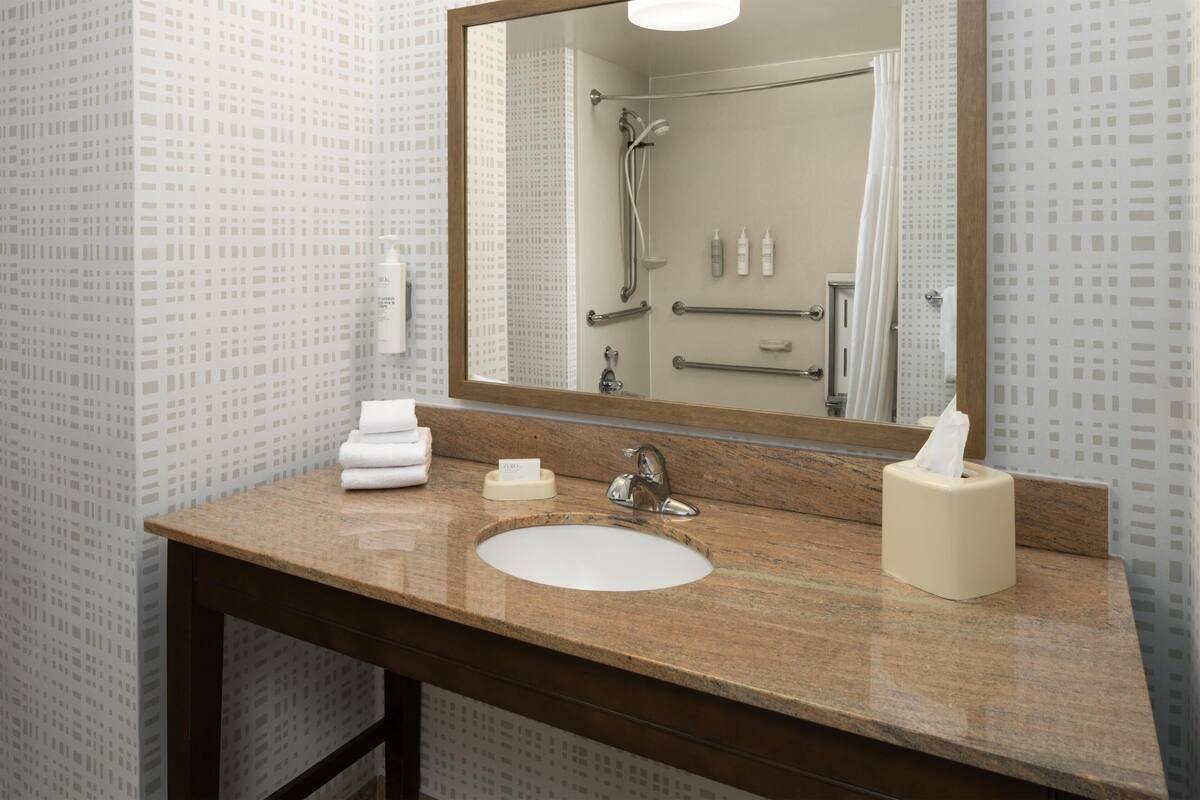 A bathroom with a marble sink, a large mirror, a towel dispenser, and a shower area.