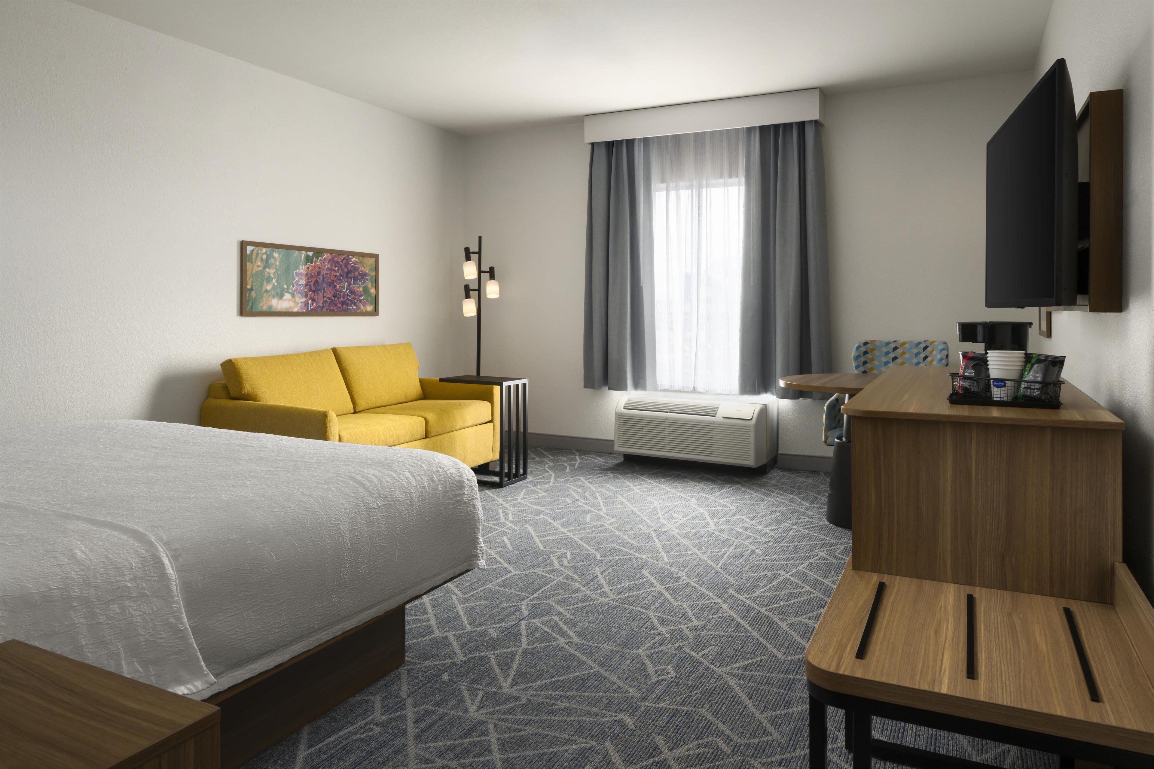 Une chambre d’hôtel comprenant un lit, un canapé, un bureau, une télévision, une fenêtre avec des rideaux et un radiateur.