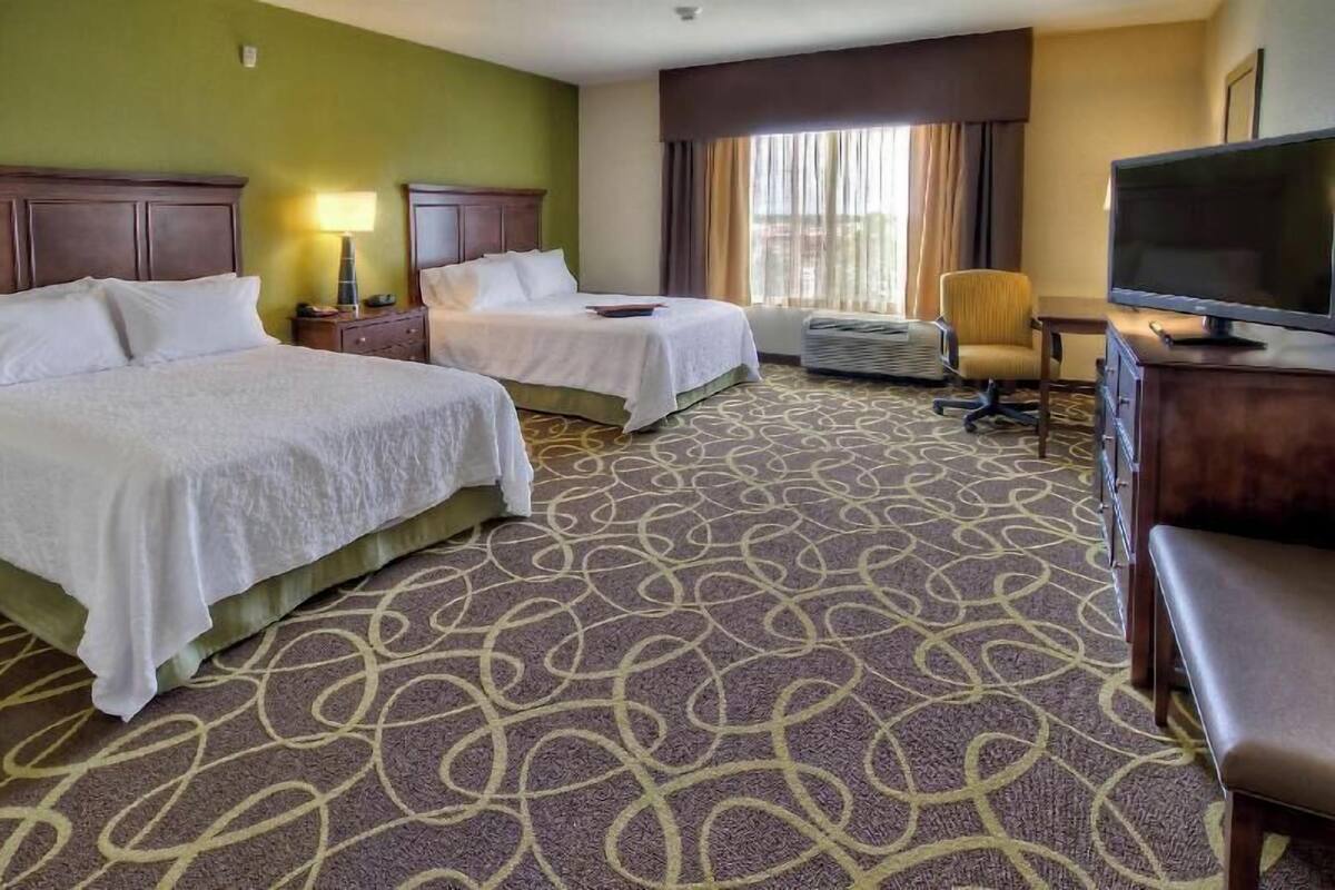 A hotel room with two beds, a television, a desk, and a chair.