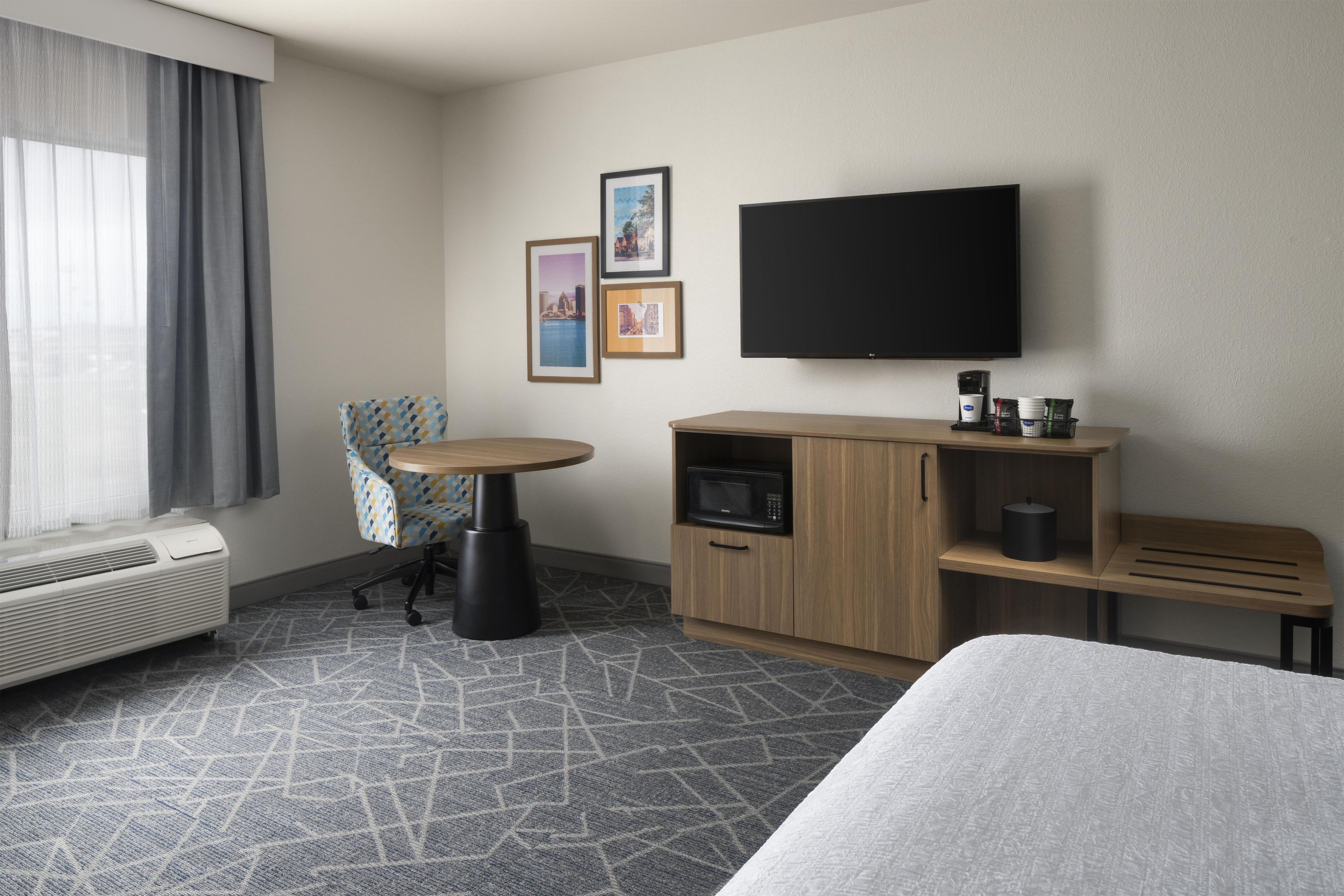 Une chambre d’hôtel équipée d’un lit, d’un bureau avec une chaise, d’un téléviseur à écran plat, d’une machine à café et d’un four à micro-ondes.