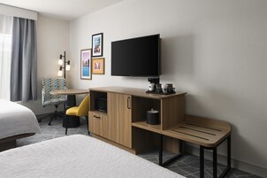 Habitación de hotel con cama, escritorio con televisor de pantalla plana, silla y cafetera.