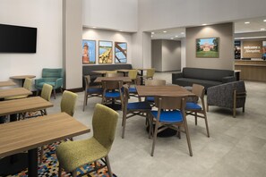 A hotel lobby with multiple seating areas, including tables and chairs, a reception desk, and artwork on the walls.